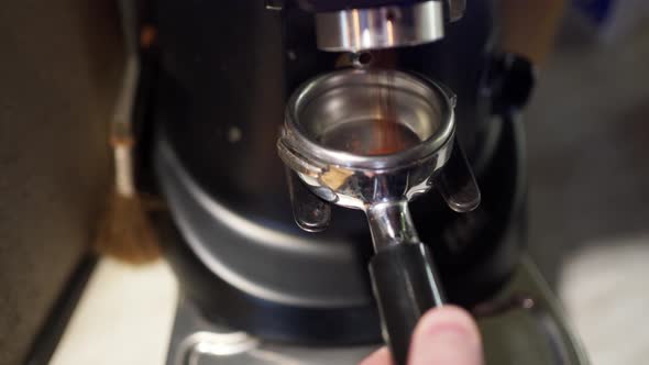 the Barista's Hand Puts the Naked Filter Holder Into a Professional Coffee Grinder and Starts