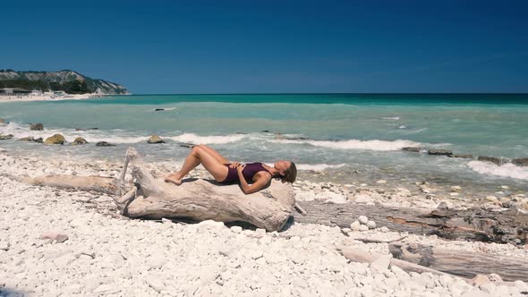 Slow motion: Woman relaxing on white gravel beach turquoise water Conero riviera coastline Italy tra