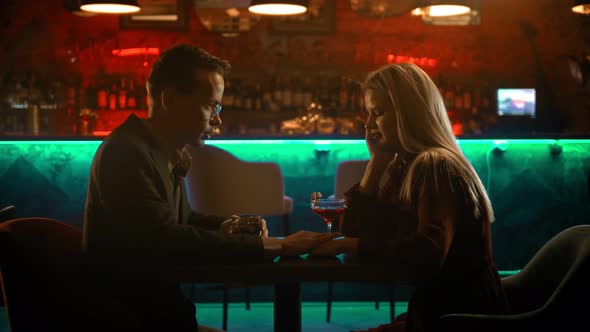 A Bewitching Couple Having a Date in the Bar - a Man Holding Woman's Hand and Making Her Shy