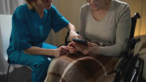 Female Nurse Helping Wheelchair Clinic Patient to Use Smartphone, Support