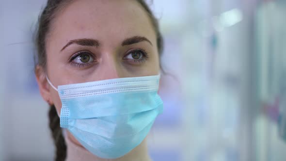 Headshot Portrait of Young Beautiful Female Doctor in Coronavirus Face Mask Looking Away with Brown