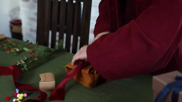 Woman in sweater is wrapping a Christmas gift in eco style in cloth