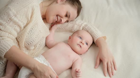 Beautiful Smiling Mother Gently Stroking and Looking on Her Little Baby Boy Lying Next to Her in Bed