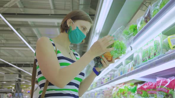  Lady in mask holding fresh salad in hands in the supermarket
