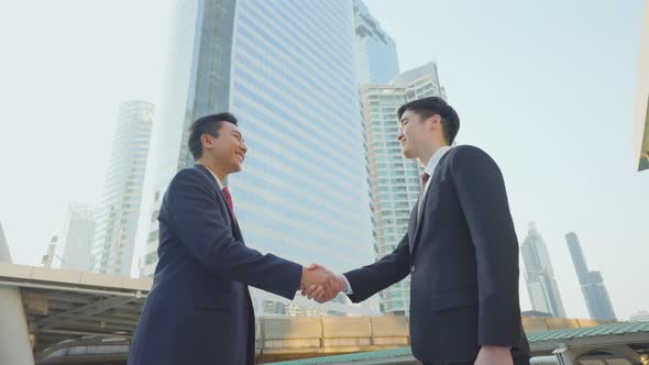 Asian businessman make handshake in city building after business deal agreement in the background.