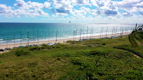 A beautiful drone shot flying the coast of Delray Beach, FL with hobie cat sailboats and a kite surf