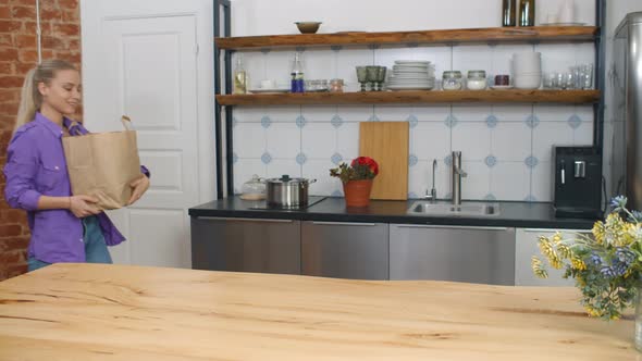 Young Woman Unpacking Bags with Groceries in Kitchen