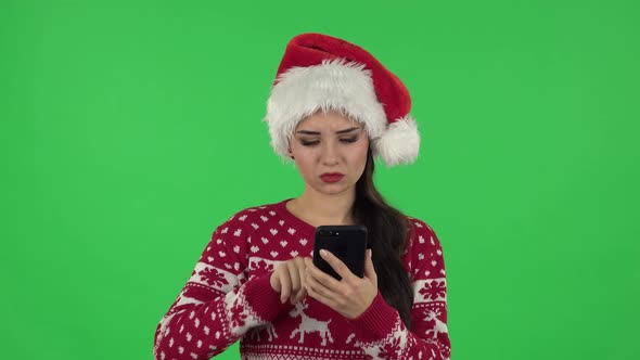 Portrait of Sweety Girl in Santa Claus Hat Is Angrily Texting on Her Phone. Green Screen