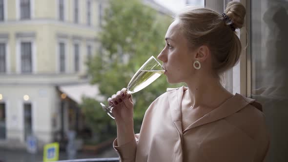 Blond Woman Drinking a Glass of Champagne on a Balcony in Budapest