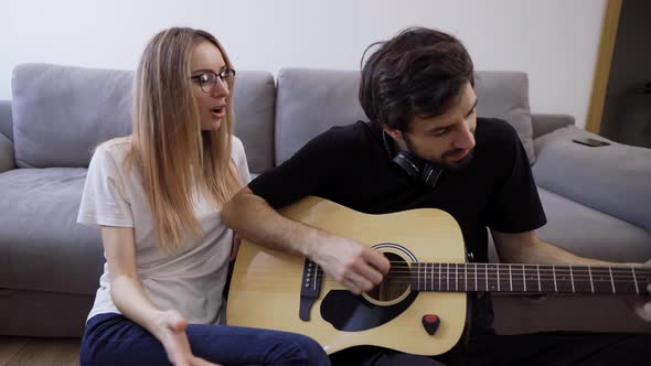 Man in Headphones Plays the Guitar at Home Happily Singing with His Girlfriend
