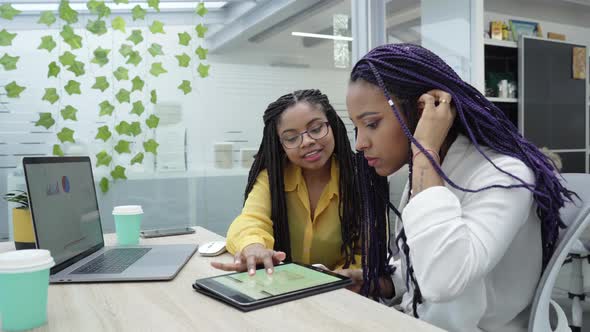 Two young black women reviewing analytical data on various electronic devices.