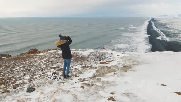 Young Woman Tourist Takes Pictures at the Top of the Cliff Around Reynisfjara Beach and Dyrholaey