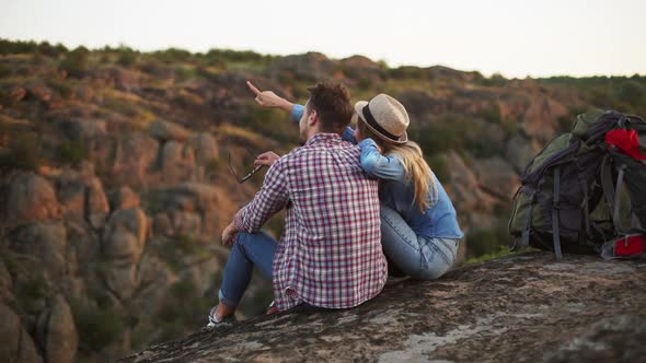 Caucasian Young Pair Sitting on Rock and Smiling