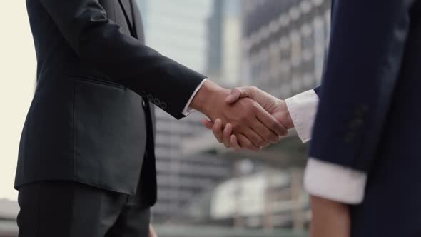 Asian businessman and businesswoman shaking hands partnership deal business while standing outside.