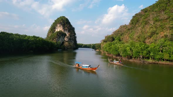 aerial of two Thai longtail boats pass each other on a green river in Krabi Town Thailand on a sunse