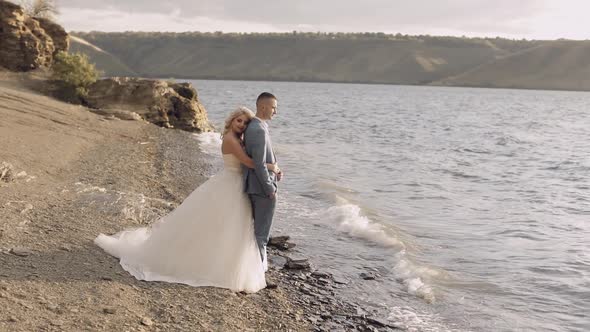 Newlyweds Stand on the Riverbank, The Bride Hugs the Groom, Wedding Couple