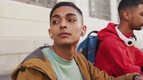 Two mixed race male friends wearing headphones, listening to music in the street