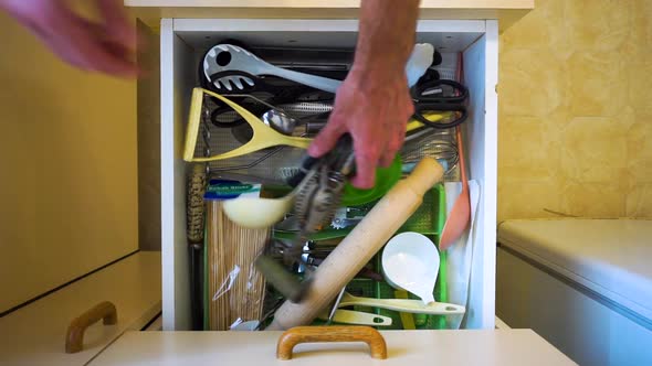 Top down view as hands open kitchen draw, search through mess of utensils and then close draw.