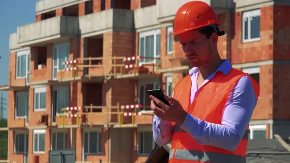 Construction Worker Works on the Smartphone in Front of Building Site