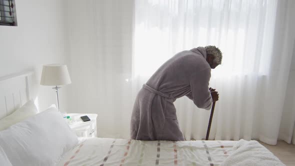 Senior man holding his walking stick while sitting on bed at home