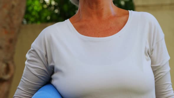 Smiling senior woman holding yoga mat in garden 4k