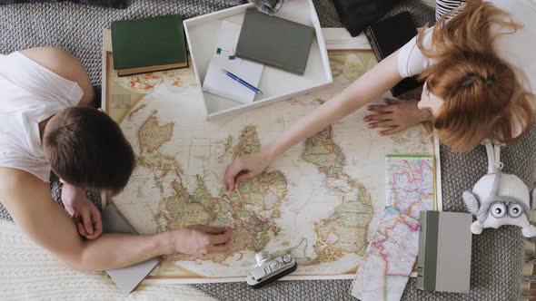 Man and Woman Are Planning Vacation Using a World Map and Other Travel Accessories.