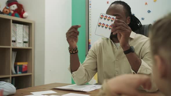 African American Teacher Teaches Teenagers Showing Cards Sitting at the Desk in the Classroom