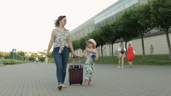 Mother and Daughter Walking Outdoors To Airport. Woman Carrying Suitcase Bag. Child and Mom Vacation