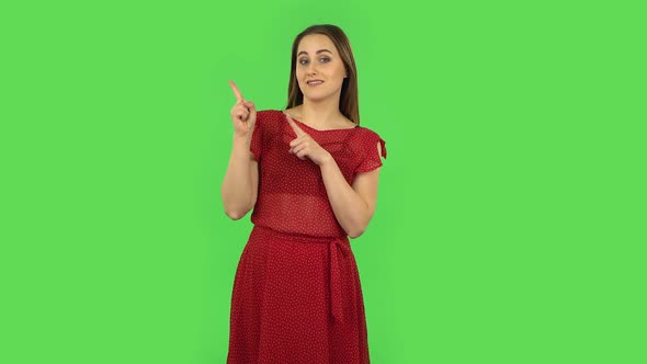 Tender Girl in Red Dress Is Talking and Pointing Side Hand for Something, Copy Space. Green Screen