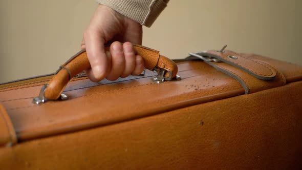 Hand lifting brown suitcase by handle close up shot