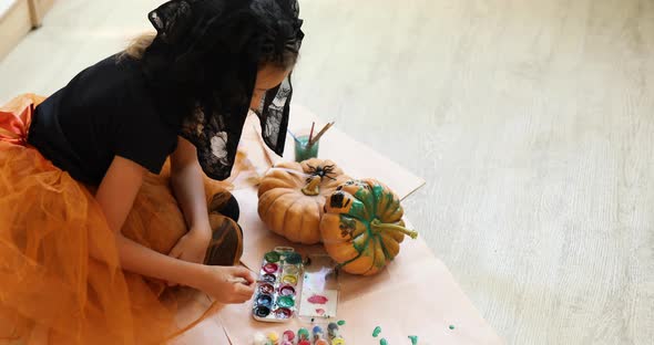 Little girl drawing face on orange Halloween pumpkin