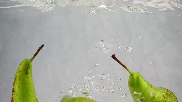 The Pears Falls Into the Water with Splashes and Bubbles in Slow Motion
