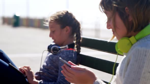 Siblings using mobile phone and digital tablet at beach