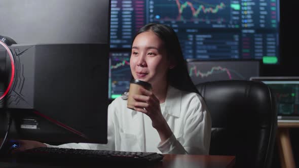 Asian Female Stock Market Broker Drinking Coffee And Working On Computer