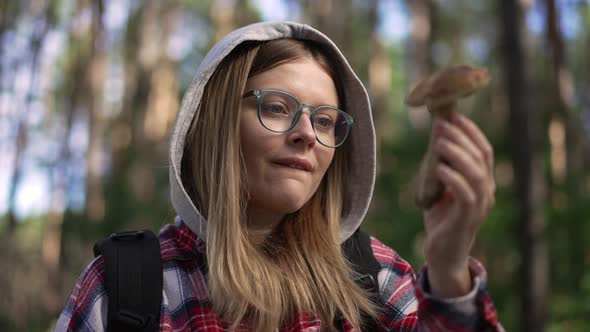 Portrait of Young Happy Woman in Eyeglasses Admiring Mushroom in Sunshine in Forest Outdoors