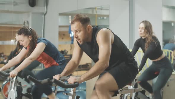 Side View of Exhausted Perspiring Man Riding Fast on Exercise Bike and Ending Exercise. Handsome