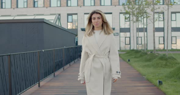 Portrait of Attractive Young Woman in Light Coat Looking To Camera While Walking at City Street