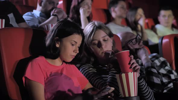 Two Girls Using Phone During Boring Film in Cinema