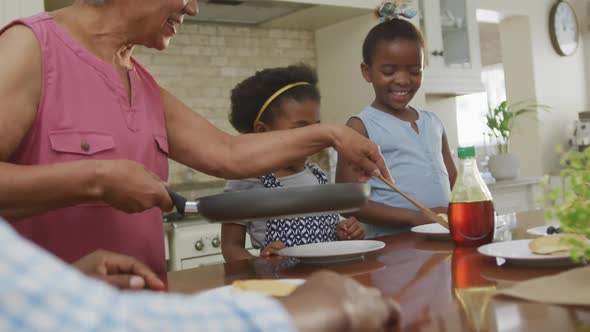 Happy african american grandparents with granddaughters having breakfast and talking