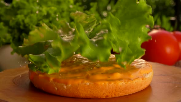 Leaf of Lettuce Falls Onto a Bun with Sauce