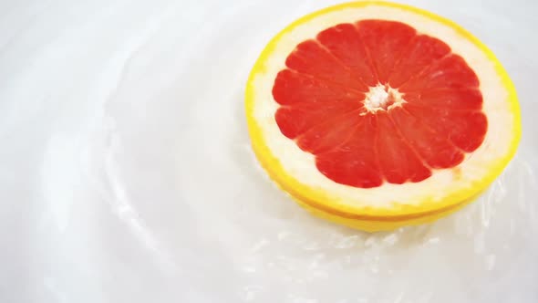 Rotating segments of ripe and juicy grapefruit in water on an white background. Slow motion.