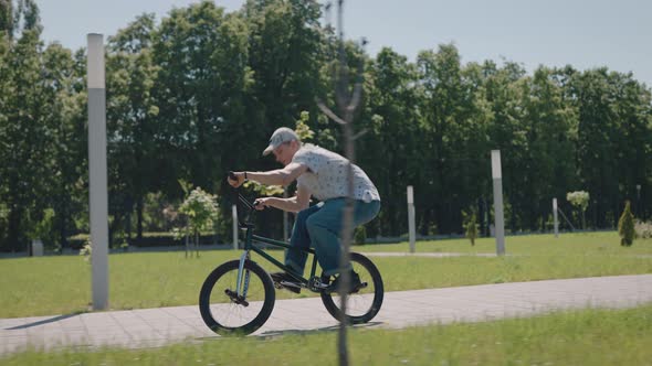 BMX Extreme Cyclist Rides Through the City Park and Performs Stunts