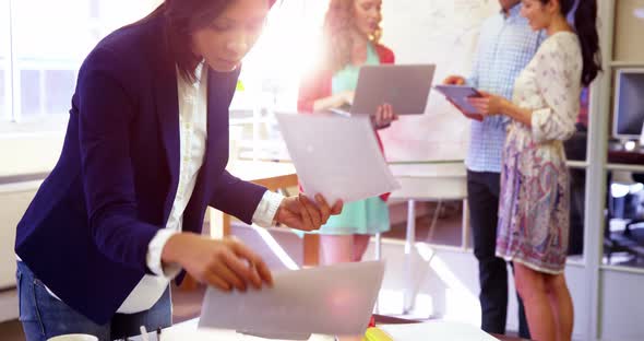 Businesswoman checking documents while coworker interacting in background