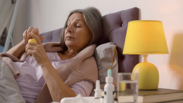 Senior Sick Woman Lying in Bed and Taking Medicine