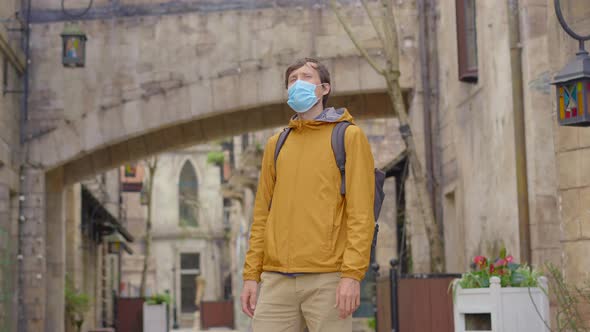 A Young Man Wearing a Face Mask Walks Between Old European Buildings