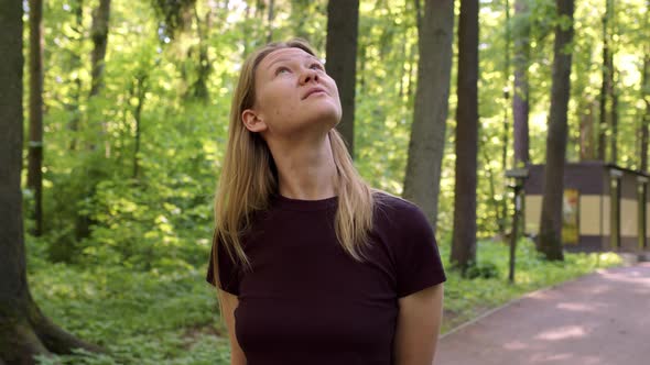 Beautiful Slender Blonde Walks Through Picturesque Green Forest at Sunset or Dawn