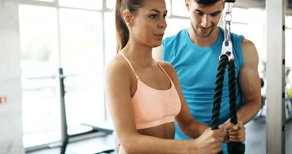 Beautiful Woman Doing Exercises in Gym with Personal Trainer