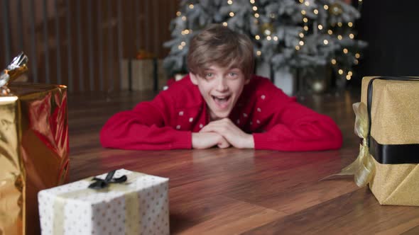 Portrait of a Happy Teenager Boy Looking Out From Under the Boxes Lying on Floor Background of