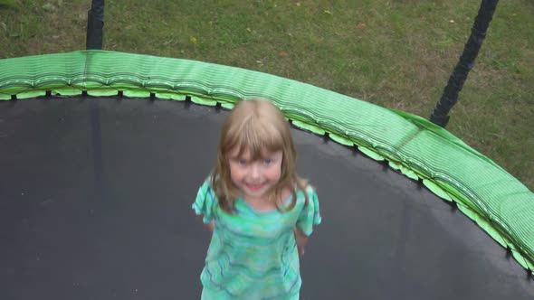 A Little Cheerful Girl in a Turquoise Tshirt is Jumping on the Trampoline