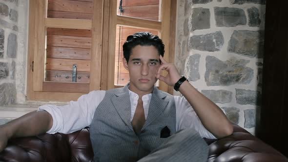 Attractive young fashion man in a suit posing in a leather chair in a restaurant. Slow motion